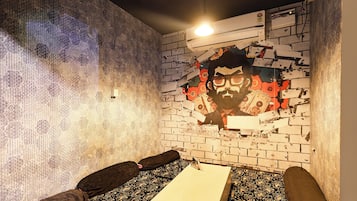 A room with a patterned wall, a bed with a white sheet, and a brick wall with a large hole revealing a graphic.
