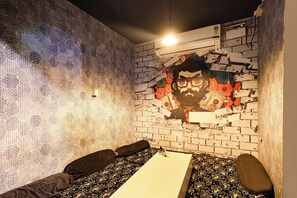 Una habitación con un papel tapiz estampado, una cama con sábana blanca y una pared de ladrillo con un gran agujero que muestra un gráfico.