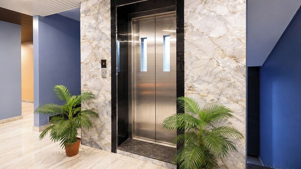 An elevator with a marble wall, two potted plants, and a blue accent wall. - Fabhotel Ssd Grand (Visakhapatnam)