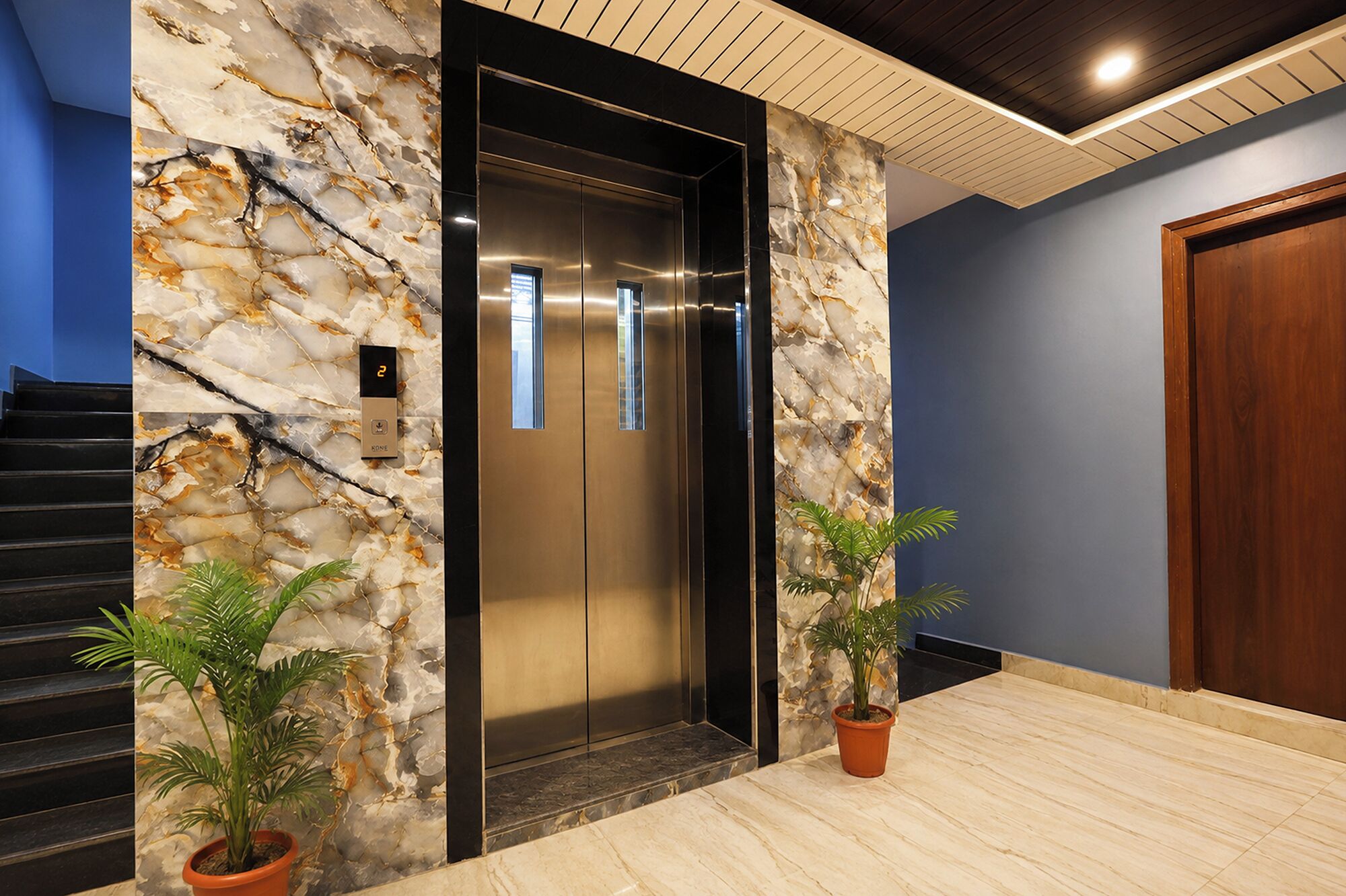 A modern elevator with a marble wall, a wooden door, and potted plants.