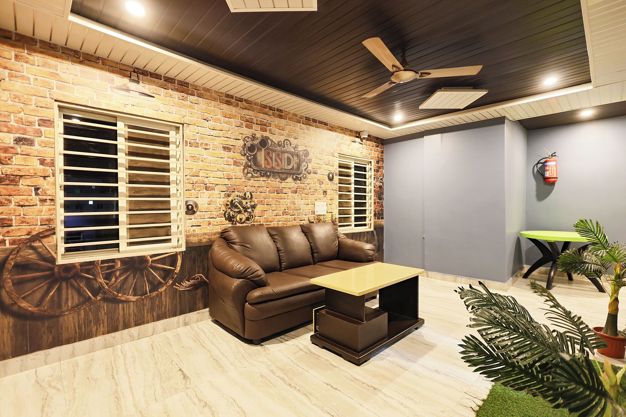 A room with a brick wall, a leather sofa, a small table, and a ceiling fan.