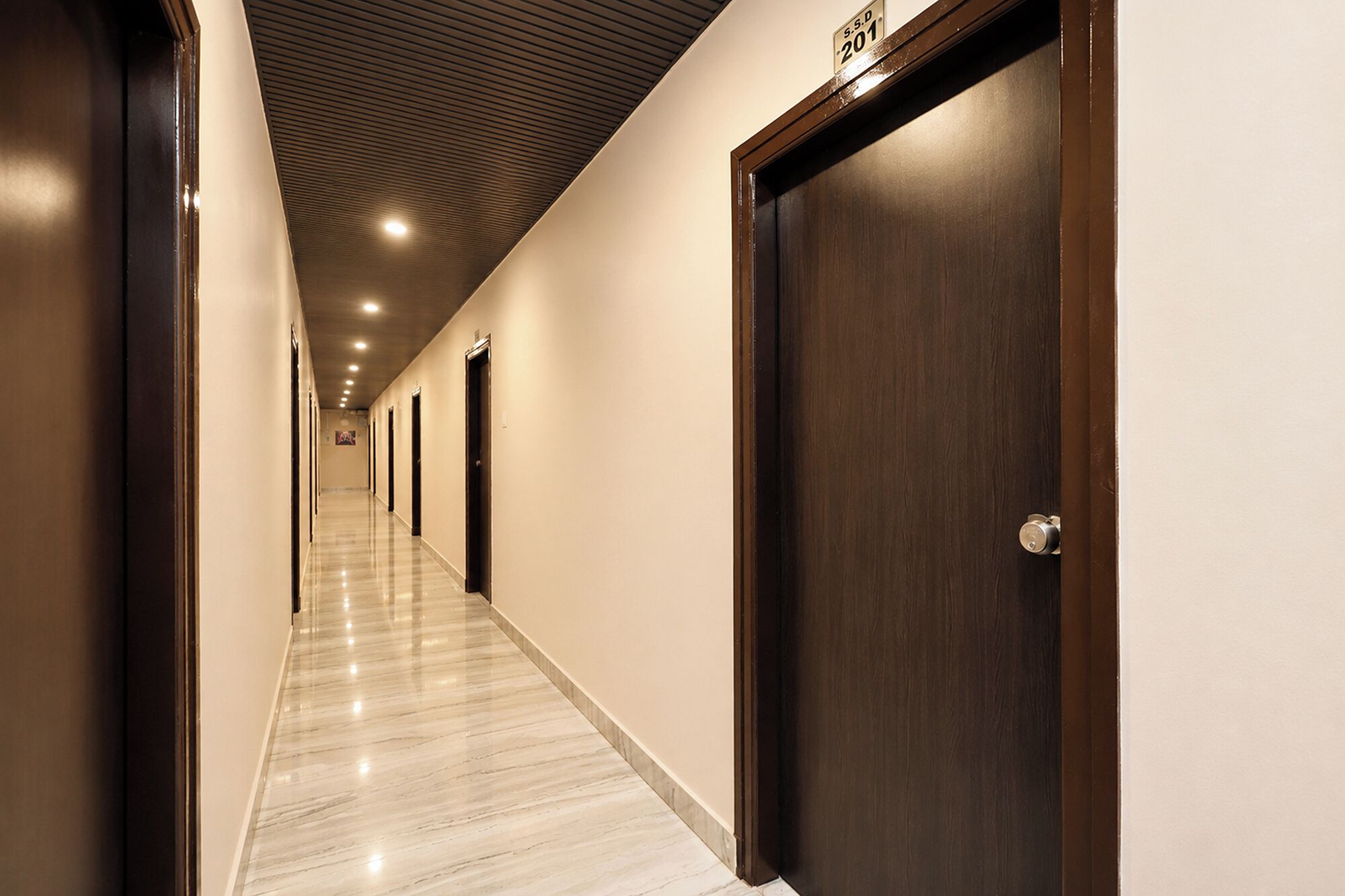 Un pasillo de hotel con puertas, suelo de mármol e iluminación empotrada en el techo.