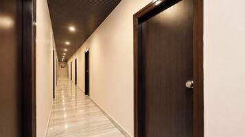 Un pasillo de hotel con puertas, suelo de mármol e iluminación empotrada en el techo.