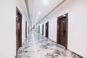 A hotel corridor with marble flooring, wooden doors, and a reception desk at the end. - Fabhotel Yash Residency Ii (Ambernath)