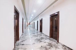 A hotel corridor with marble flooring, wooden doors, and a reception desk at the end.