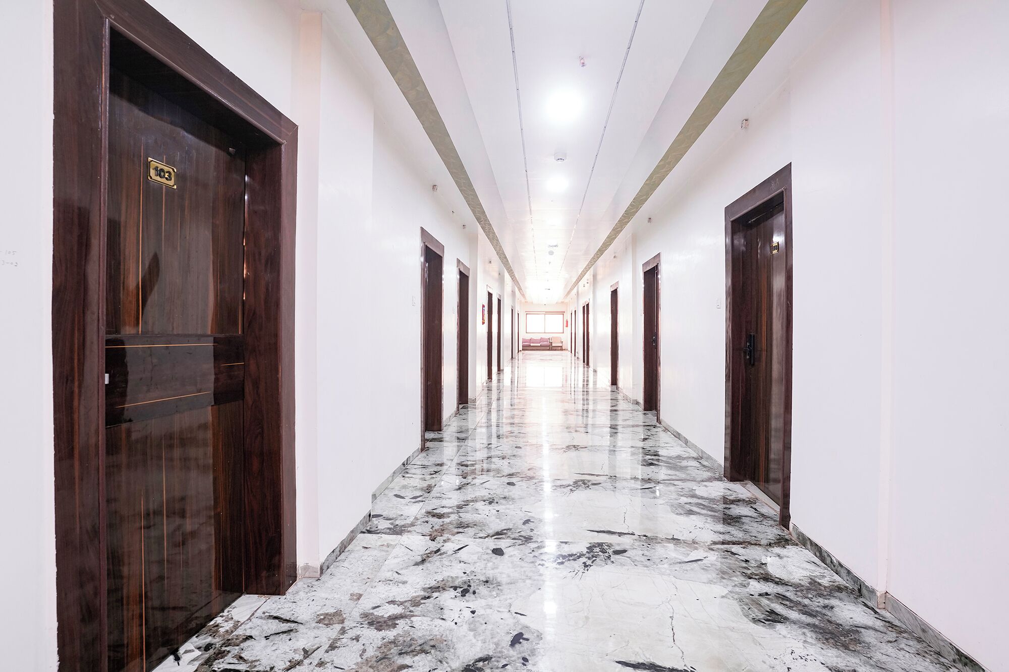 A long corridor with marble flooring and wooden doors, leading to a seating area at the end.