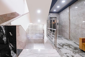 A marble staircase leading to an elevator, with a metal railing and a patterned wall. - Fabhotel Yash Residency Ii (Ambernath)