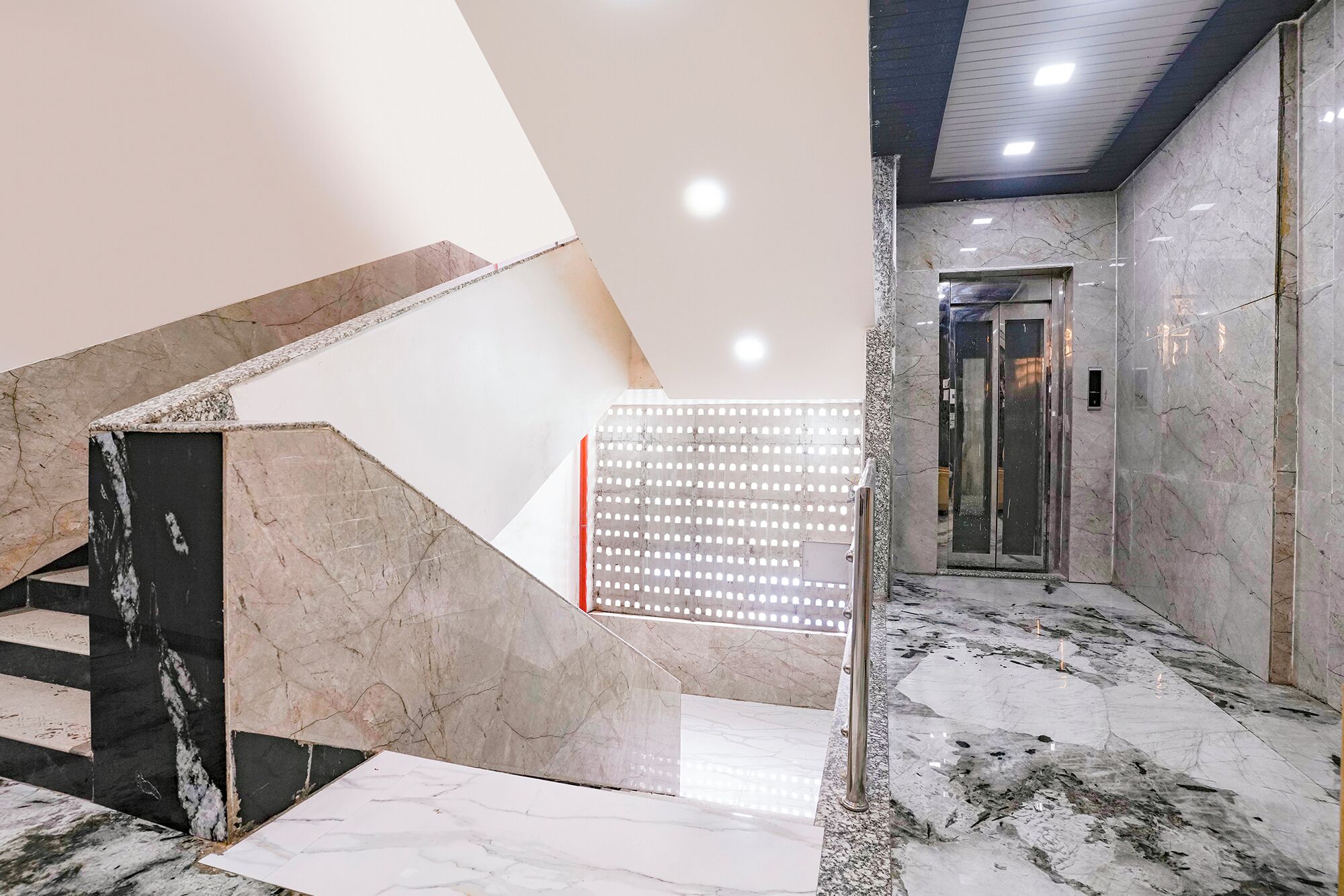 Una escalera de mármol que conduce a un ascensor, con un moderno elemento de iluminación en el techo.