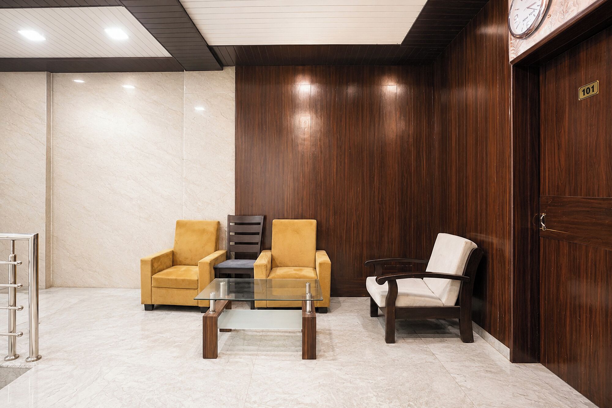 A lobby with two armchairs, a glass coffee table, and a wooden door with a number plaque.