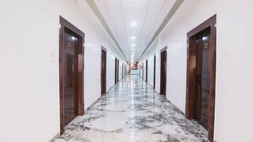A long, narrow hotel corridor with marble flooring and wooden doors on both sides.