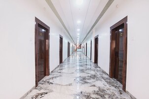 A long, narrow hotel corridor with marble flooring and wooden doors on both sides.