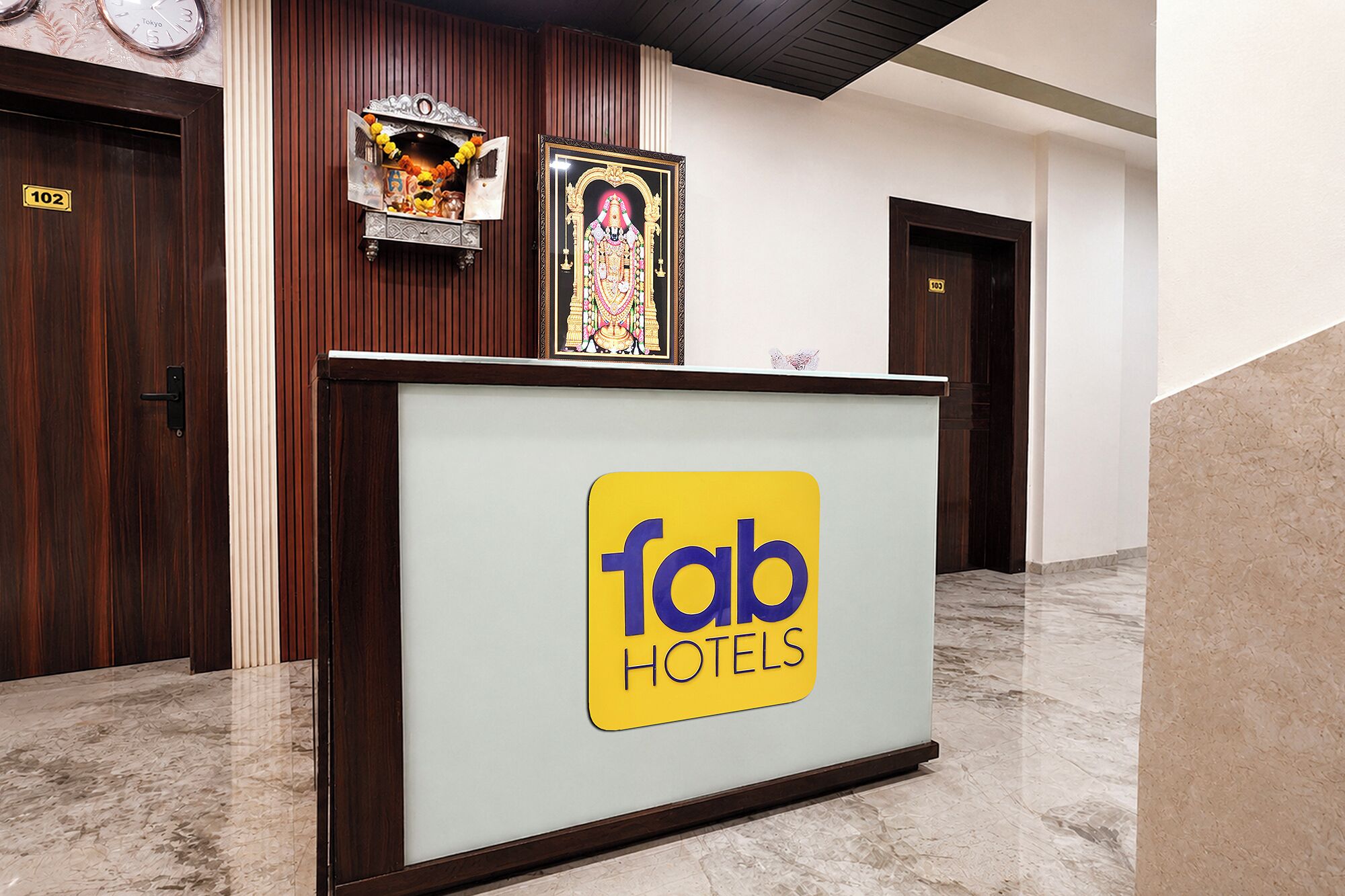 A hotel reception desk with a 'fab hotels' sign, a clock, and a small shrine with offerings.