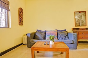 A living room with a sofa, a coffee table, a plant, and a painting on the wall. - FabHotel Bounty Yatra (Arpora)
