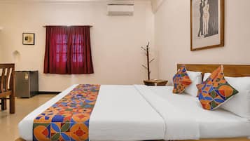 Habitación de hotel con cama, mesita de noche, una silla, una pequeña mesa y aire acondicionado instalado en la pared.