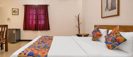 A hotel room with a bed, a nightstand, a chair, a small table, and a wall-mounted air conditioner.