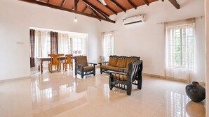 A spacious room with a high ceiling, a dining area with wooden furniture, and large windows allowing natural light. - Fabhotel Bounty Yatra (Arpora)