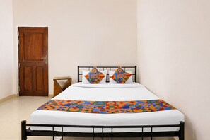 Een enkel bed met een metalen frame, een houten deur en een klein houten krukje.