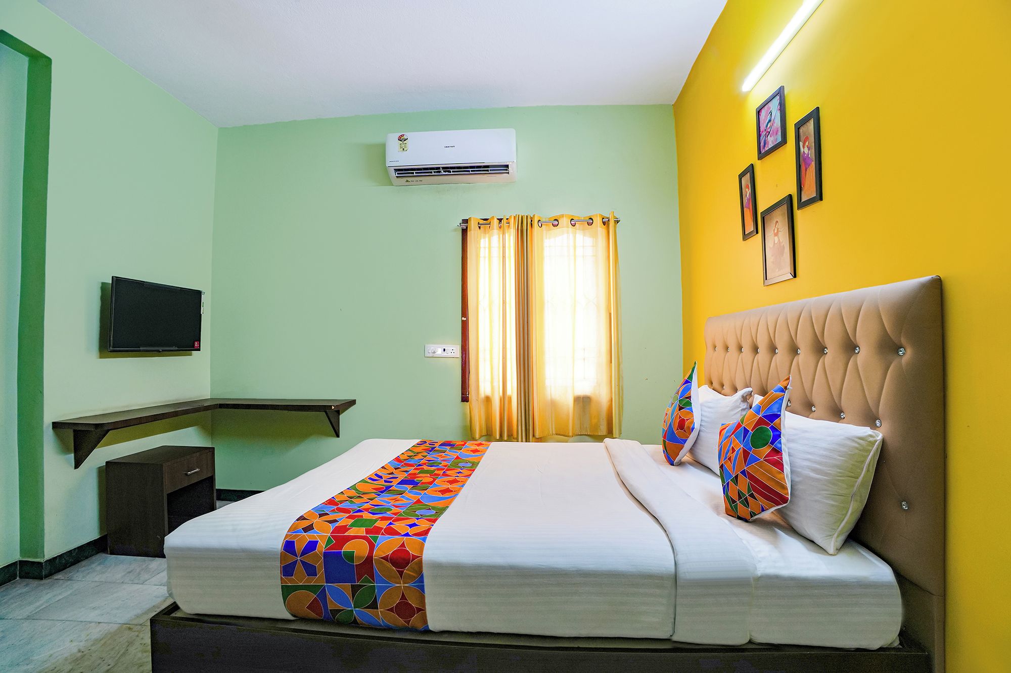 A hotel room with a bed, a television, an air conditioning unit, and a window with curtains.