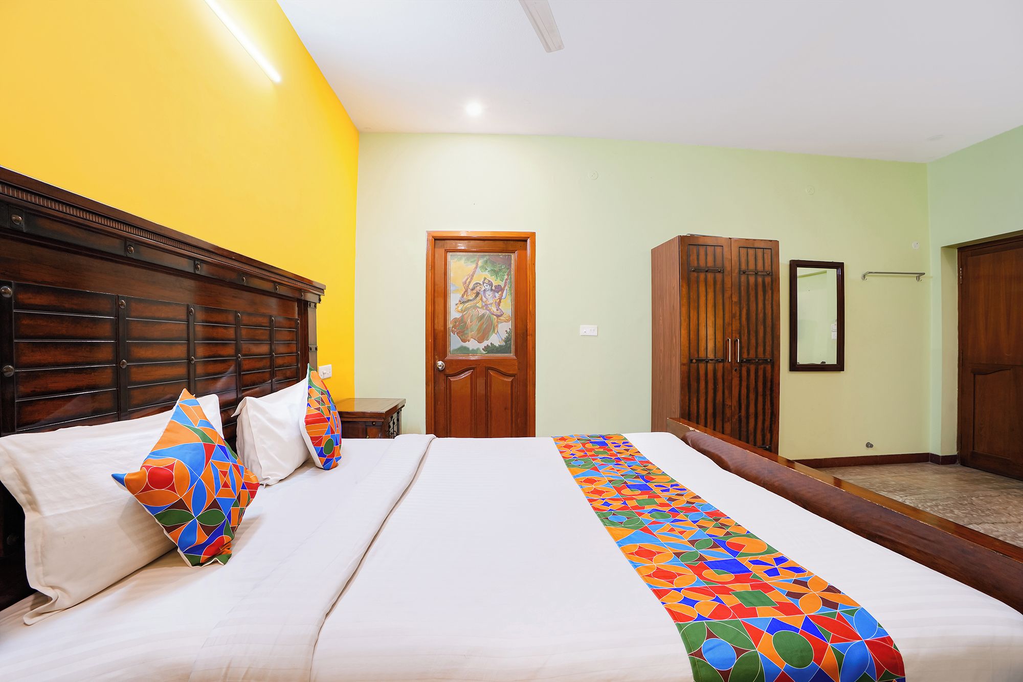 A hotel room with a large bed, a wooden headboard, a door with a painting, and a wardrobe.