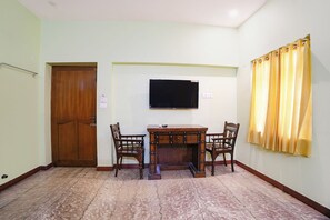A room with a wooden desk, two chairs, a television mounted on the wall, a door, and a window with curtains. - Fabhotel Zamindar Garden (Puducherry)