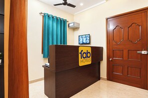 A reception desk with a 'fab hotels' sign, a ceiling fan, a wall-mounted air conditioner, and a wooden door. - FabHotel Zamindar Garden (Puducherry)