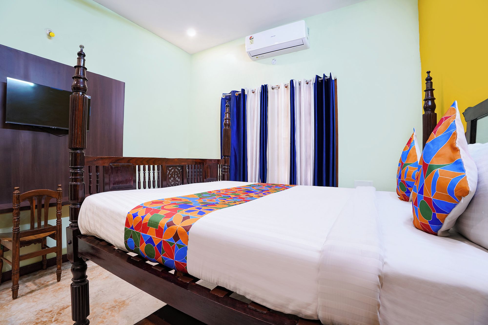 A hotel room with a bed, a television, an air conditioning unit, and a window with curtains.