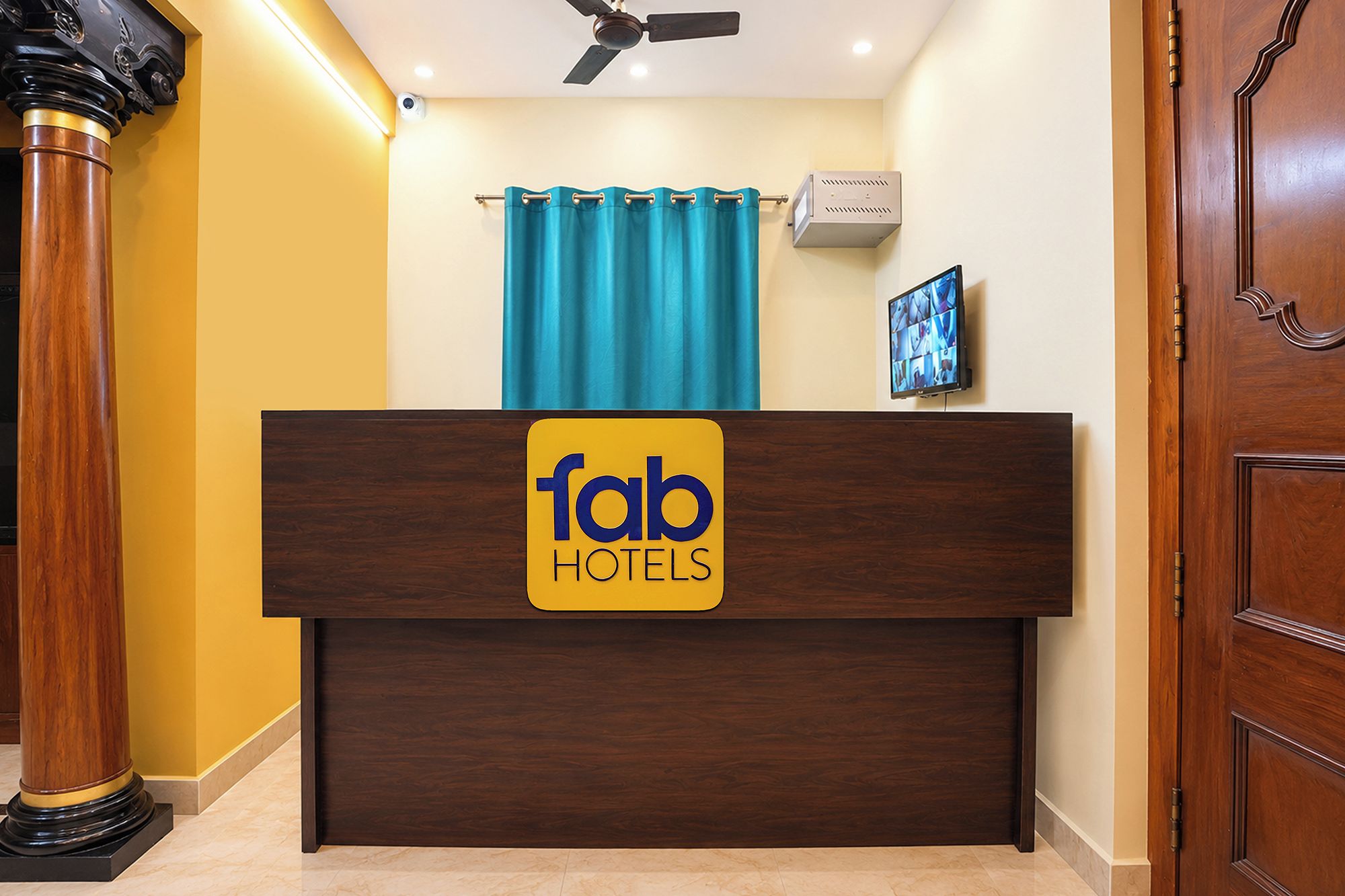 Una mesa de recepción con un letrero de 'fab hotels', un ventilador de techo, una cortina azul y un televisor montado.