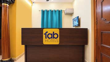 Una mesa de recepción con un letrero de 'fab hotels', un ventilador de techo, una cortina azul y un televisor montado.