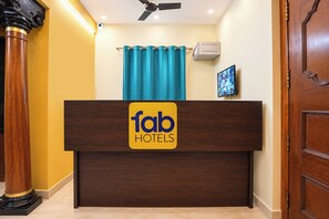 A reception desk with a 'fab hotels' sign, a ceiling fan, a blue curtain, and a mounted television. - Fabhotel Zamindar Garden (Puducherry)
