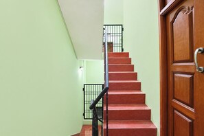 A staircase with red steps leading to a landing, flanked by light green walls and a wooden door with a brass handle. - FabHotel Zamindar Garden (Puducherry)