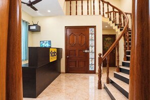 A hotel reception desk with a 'fab hotels' sign, a wooden staircase, and a door with a stained glass window. - FabHotel Zamindar Garden (Puducherry)