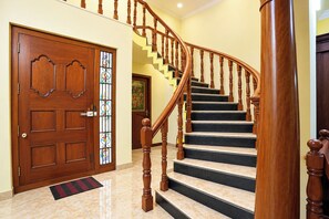 A wooden staircase with a handrail, leading to a landing with a door and a stained glass window. - FabHotel Zamindar Garden (Puducherry)