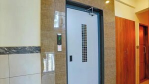 Een hotel lift met een digitaal scherm waarop het getal 3 staat, een betegelde wand en een houten deur.