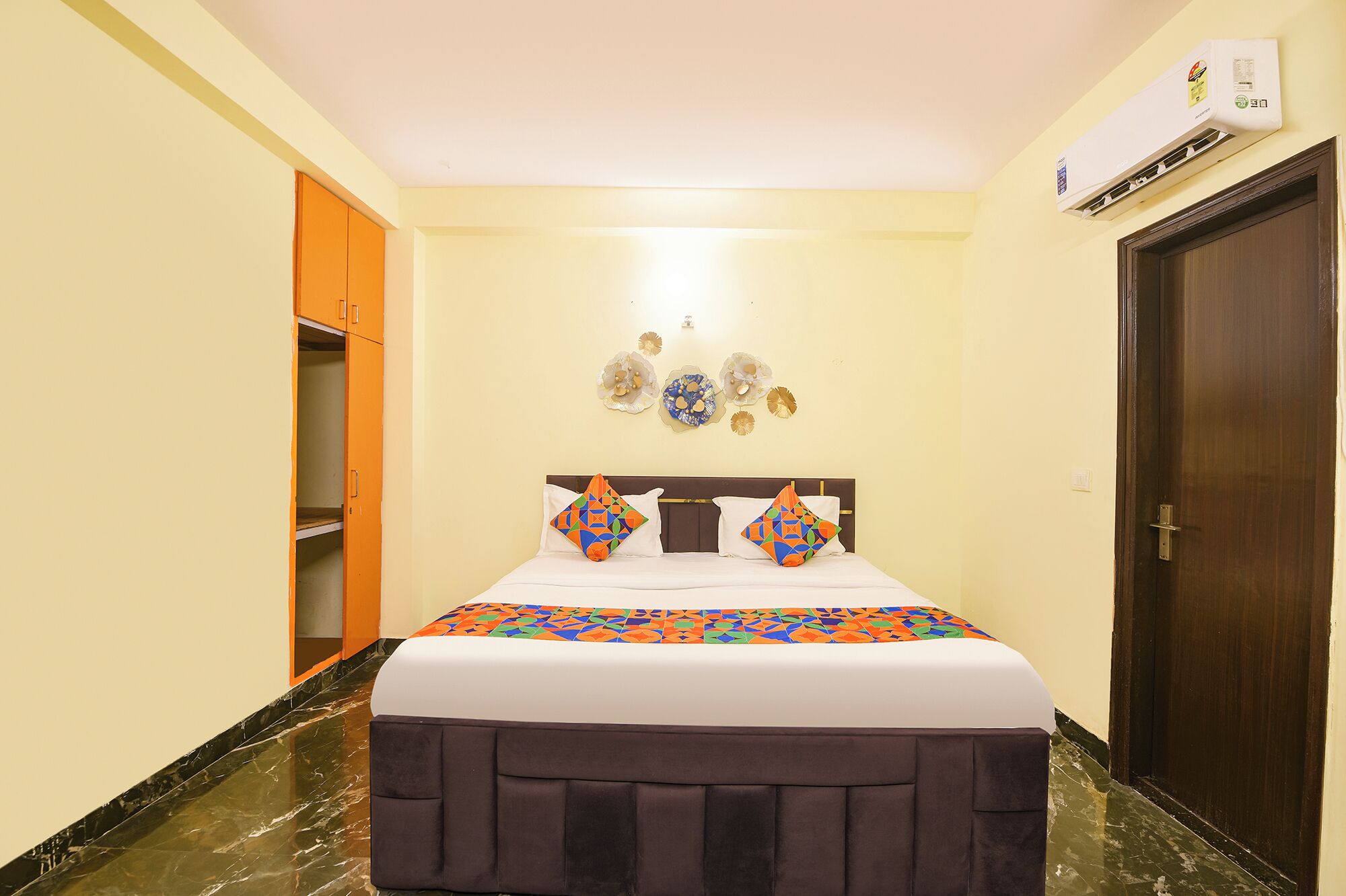 A hotel room with a bed, a wardrobe, decorative wall art, and an air conditioning unit.