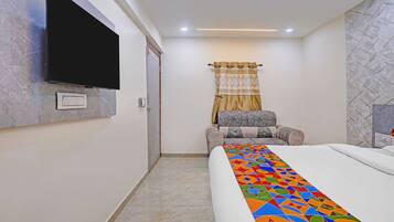 A hotel room with a bed, a television mounted on the wall, a patterned curtain, and a chair.