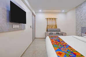 A hotel room with a bed, a television mounted on the wall, a patterned curtain, and a chair. - FabHotel Sky Inn I (Ahmedabad)