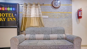 A hotel room with a sofa, a clock, a fire extinguisher, and a curtain. - Fabhotel Sky Inn I (Ahmedabad)