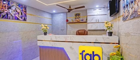 Un mostrador de recepción de hotel con encimera de mármol, ventilador de techo y cartel de 'fab hotels'.