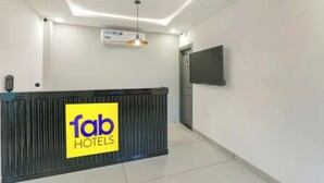 A hotel reception area with a reception desk, a flat-screen TV mounted on the wall, and a ceiling light fixture. - Fabhotel Bsa (Lucknow)