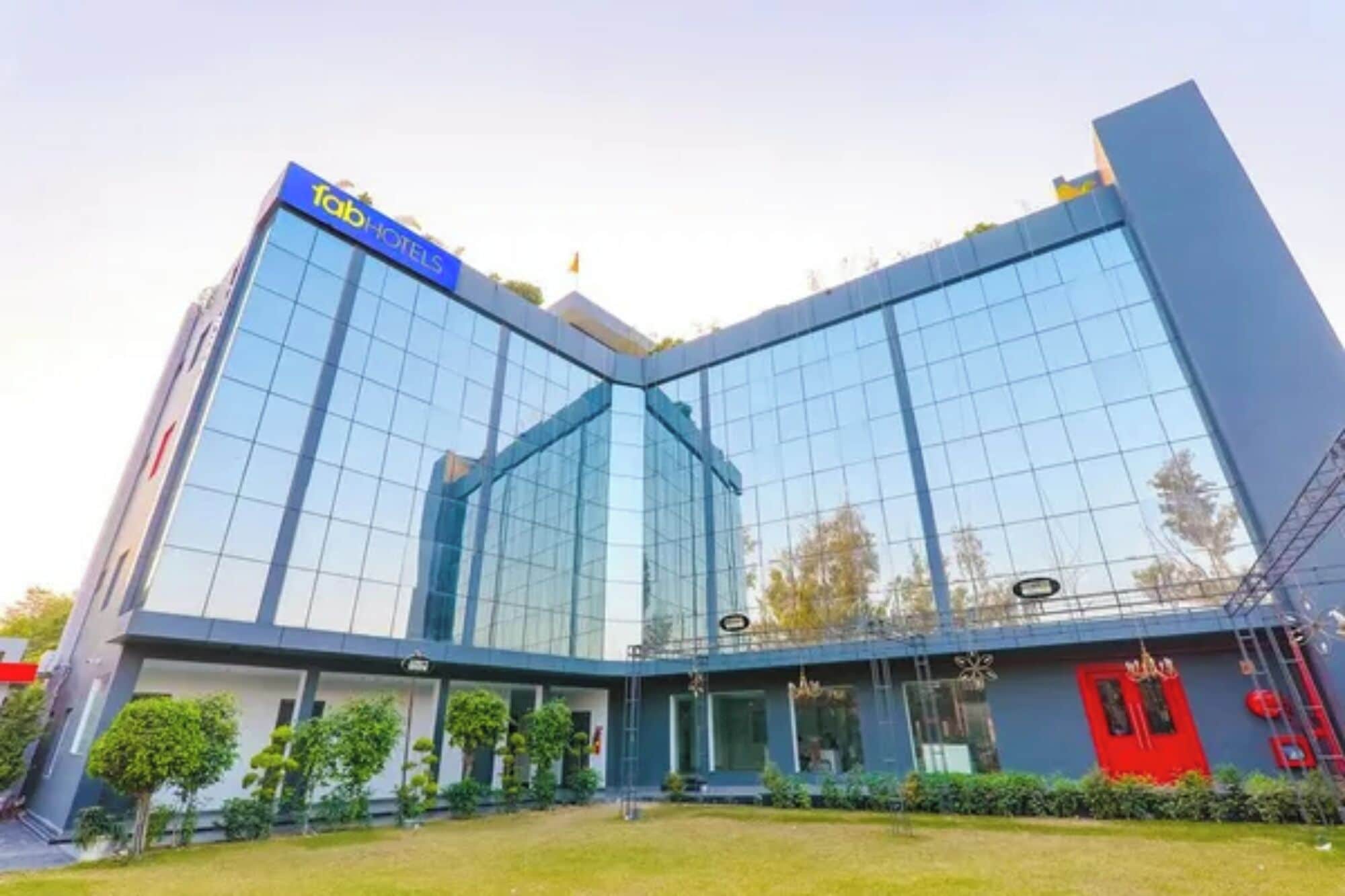 A modern hotel with a glass facade, a prominent blue sign, and a red door.