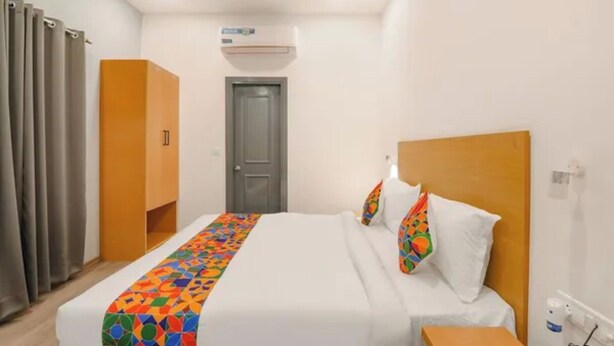 A hotel room with a bed, a bedside table, a wardrobe, and an air conditioning unit. - Fabhotel Bsa (Lucknow)
