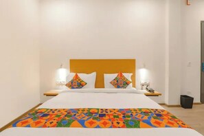 A hotel room with a bed, two bedside tables, a nightstand, a lamp, and a trash bin. - FabHotel Bsa (Lucknow)