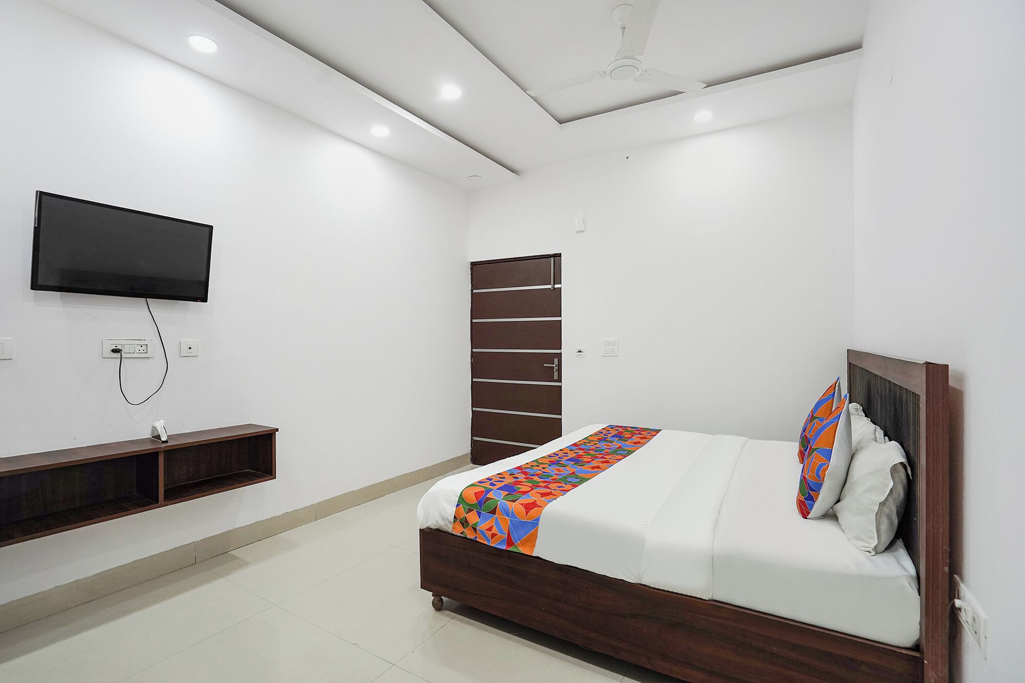 A bedroom with a bed, a TV mounted on the wall, and a door.