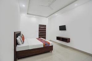 A bedroom with a bed, a TV, a ceiling fan, and a wooden wardrobe. - Fabhotel Luxury Stay (Noida)