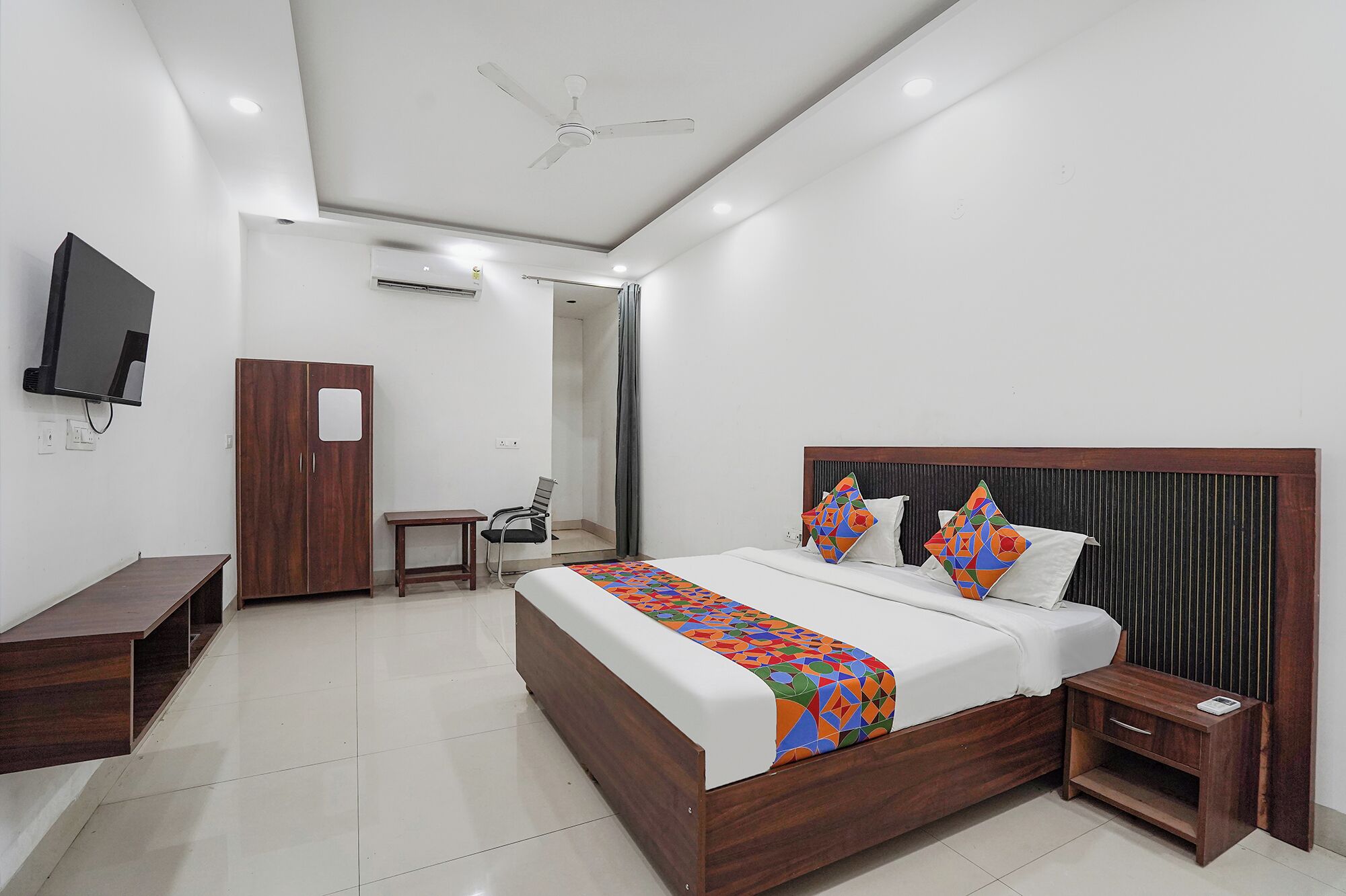 A hotel room with a bed, bedside table, TV, wardrobe, and a desk.