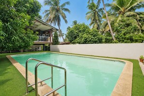 A swimming pool with a metal ladder, surrounded by a white wall and lush greenery, including palm trees. - FabHotel Manvin's Inn (Panaji)