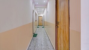 A corridor with a wooden door on the right, a green mat at the entrance, and a tiled floor.
