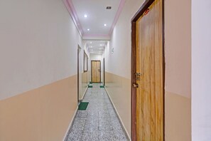 A corridor with a wooden door on the right, a green mat at the entrance, and a tiled floor. - FabHotel Manvin's Inn (Panaji)
