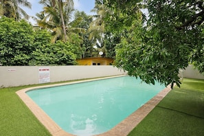 A swimming pool with a no smoking and no jumping sign, surrounded by lush greenery and a white wall. - FabHotel Manvin's Inn (Panaji)