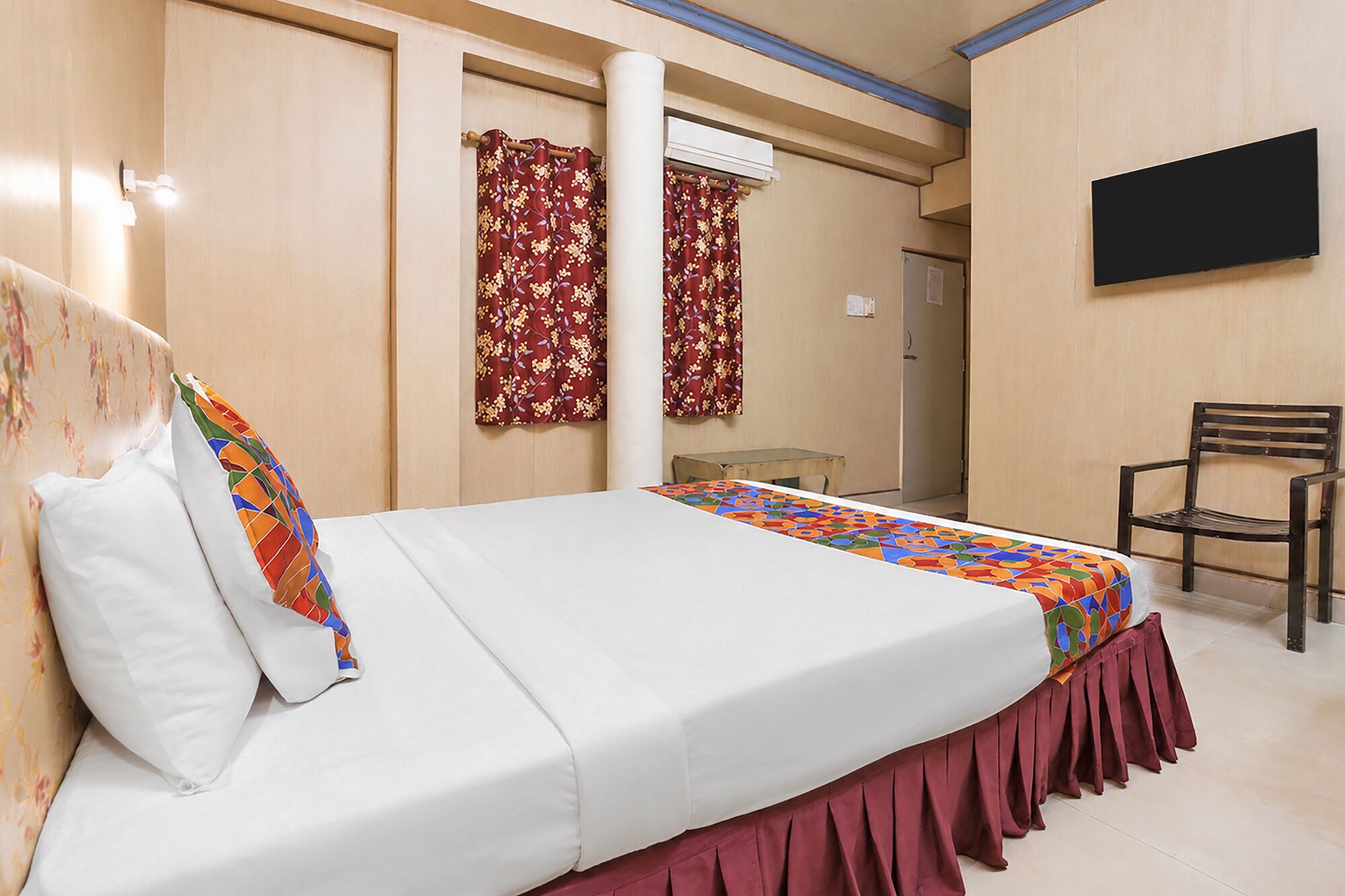 Una habitación de hotel con cama, una silla, televisor y cortinas.